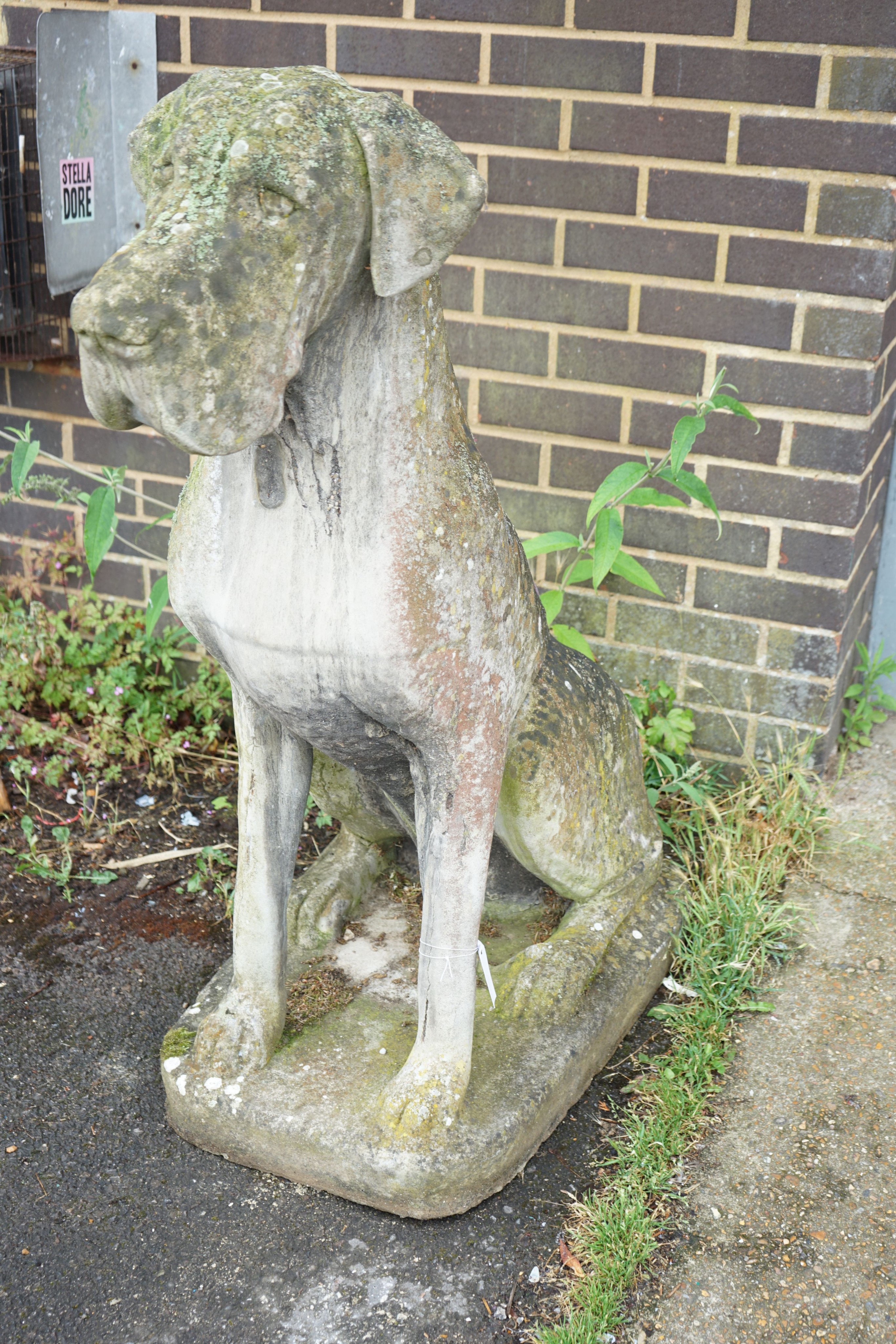 A large weathered reconstituted stone garden ornament modeled as a seated Great Dane, height 116cm